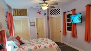 Une chambre à coucher avec un lit, un ventilateur de plafond, une télévision et une porte.