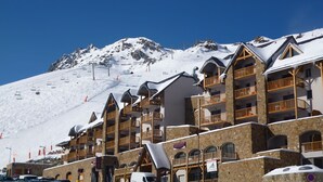 Una montaña nevada con un telesilla y una hilera de edificios de madera con balcones.