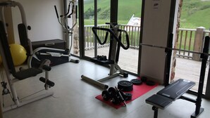A gym with exercise equipment, a bench, and a view of a green landscape through a large window.