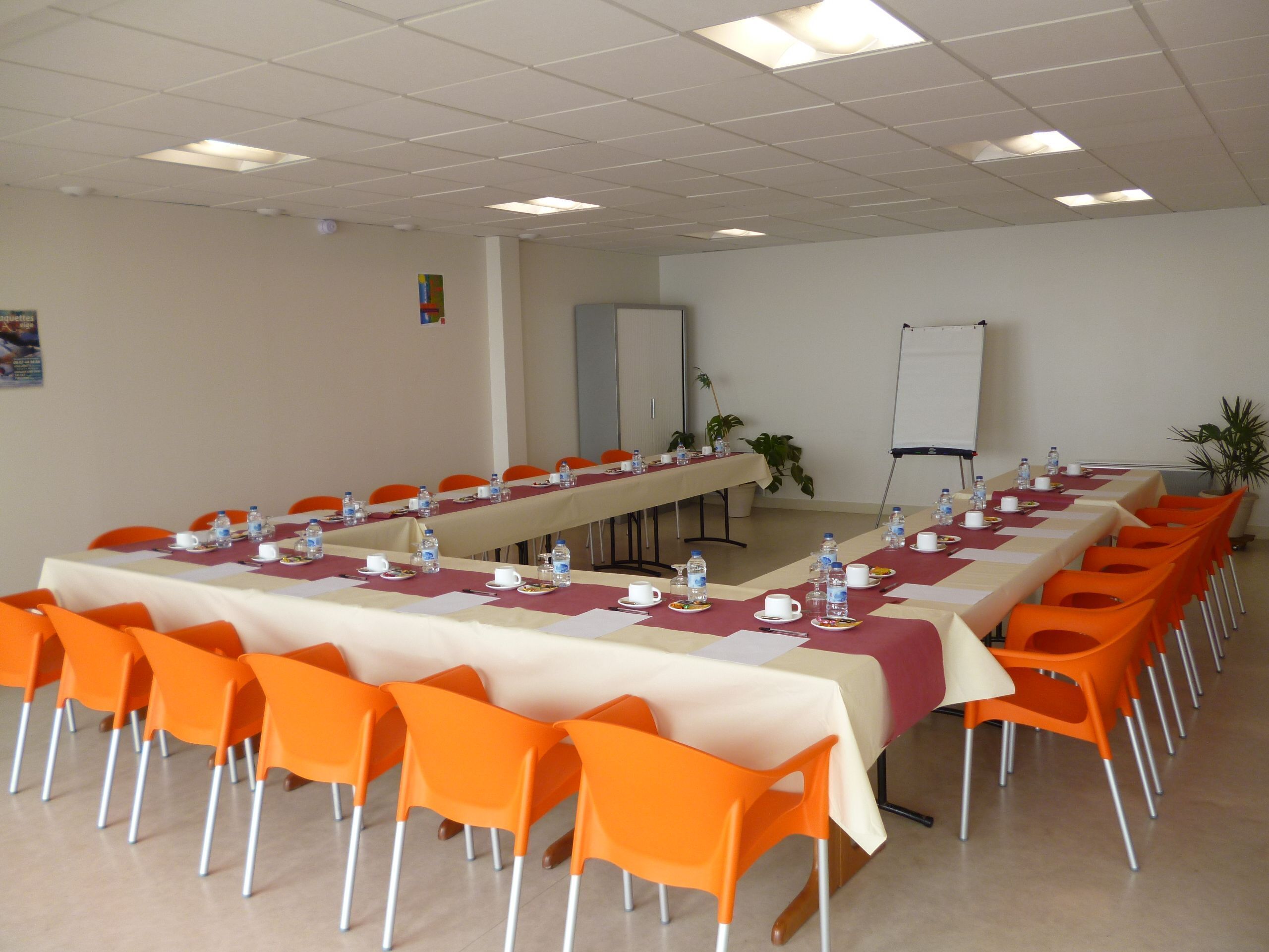 Uma sala de conferências com uma mesa comprida, cadeiras laranja e um quadro branco.