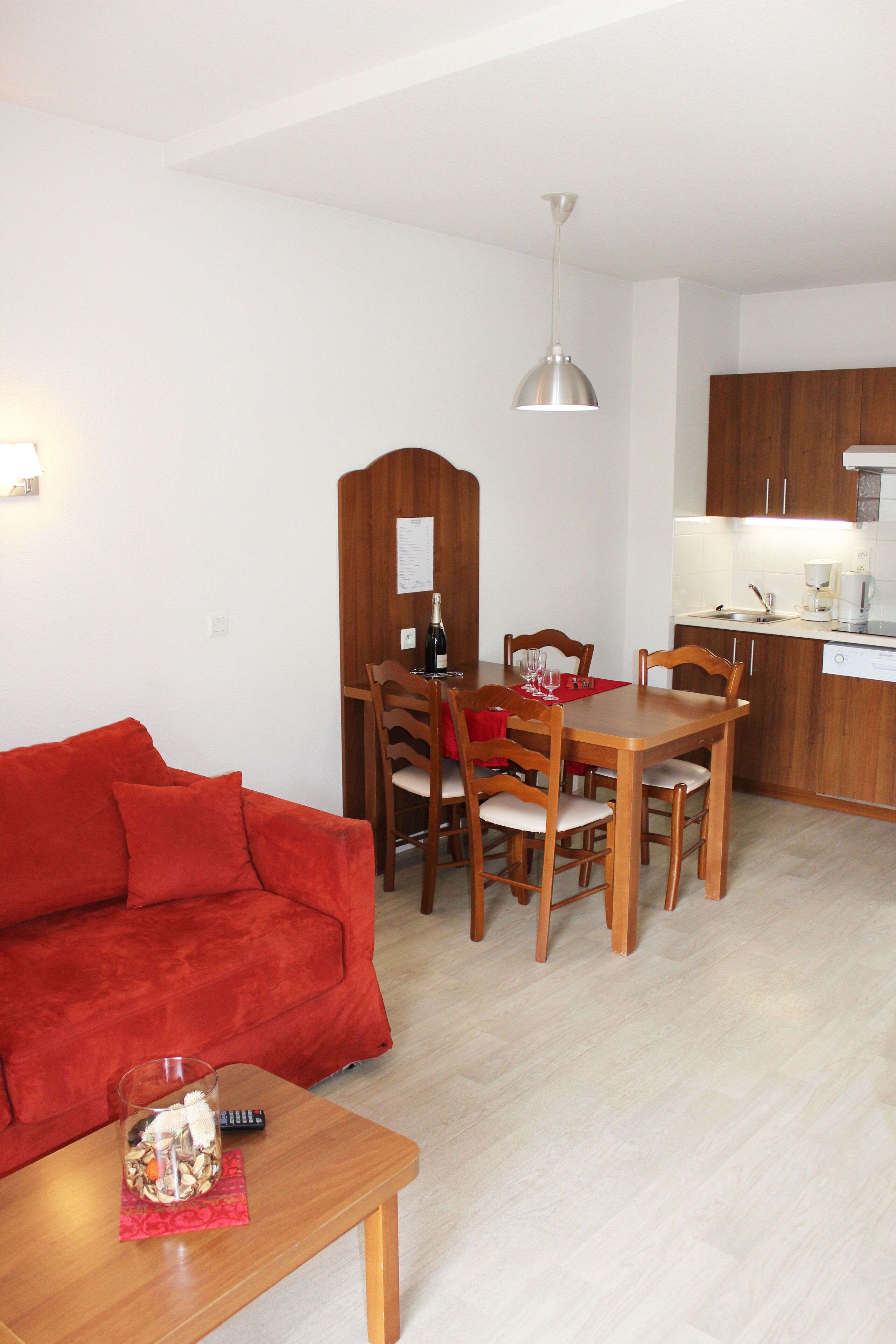 A compact living space with a dining area, a kitchen, and a red sofa.