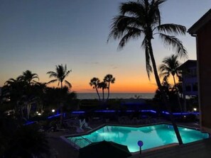 A pool area with palm trees and a sunset view. - Beach Resort- First Floor walkout to Sand! (Fort Myers Beach)