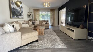 Ein modernes Wohnzimmer mit Ecksofa, Couchtisch, Fernseher und einer Deckenleuchte.