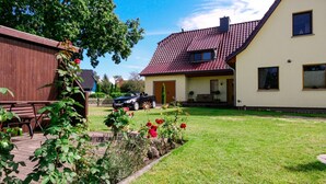 Une maison à deux étages, avec un toit recouvert de tuiles rouges, un porche et une pelouse bien entretenue.