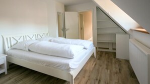 Une chambre avec un lit blanc, un plancher en bois, une armoire blanche et un escalier.