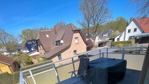 Une terrasse avec une table et des chaises, donnant sur un quartier résidentiel avec des maisons et des arbres.