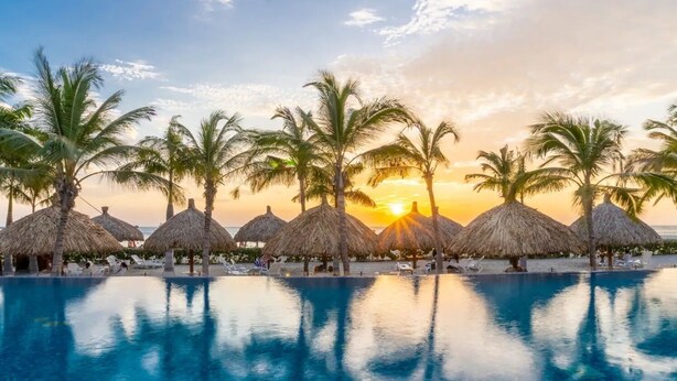 A poolside area with thatched umbrellas and palm trees, reflecting the sunset. - Exclusive Apartment 3 Bedroom in Beach Club (Santa Marta)