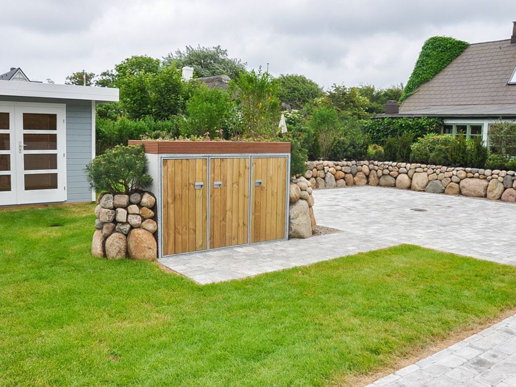 A house with a wooden garage door, a stone wall, and a paved driveway.