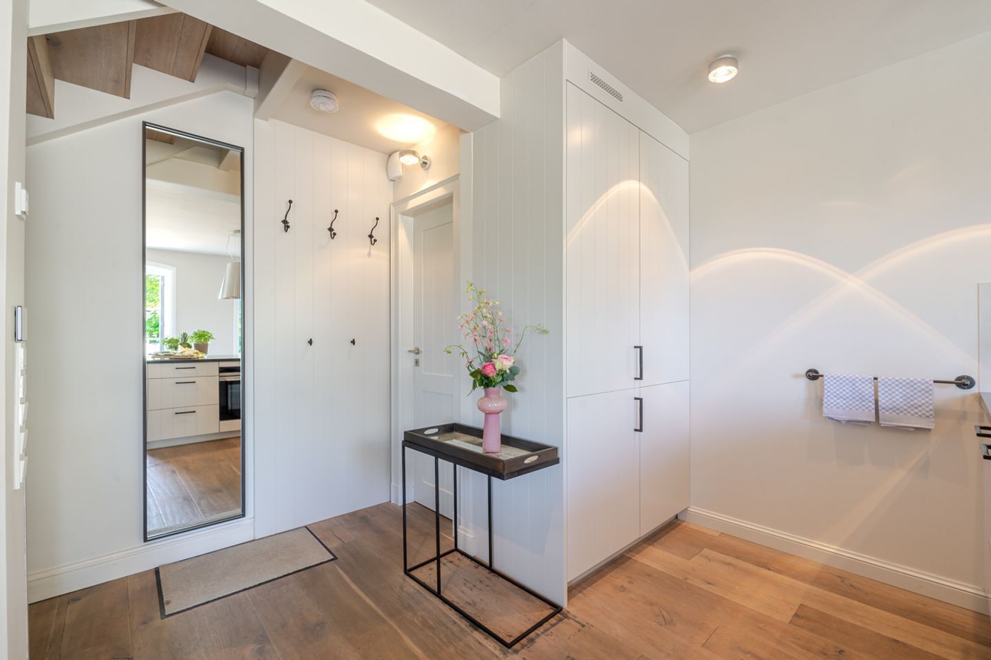 Une salle de bain moderne avec un miroir, des meubles blancs, un lavabo agrémenté d’un vase de fleurs et un porte-serviettes.