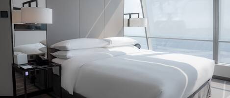 Habitación de hotel moderna con una cama grande, una mesita de noche con lámpara, un espejo y vistas a la ciudad.