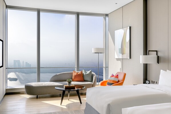 Una habitación de hotel moderna con un ventanal grande, un sofá, una silla, una cama y una mesita.