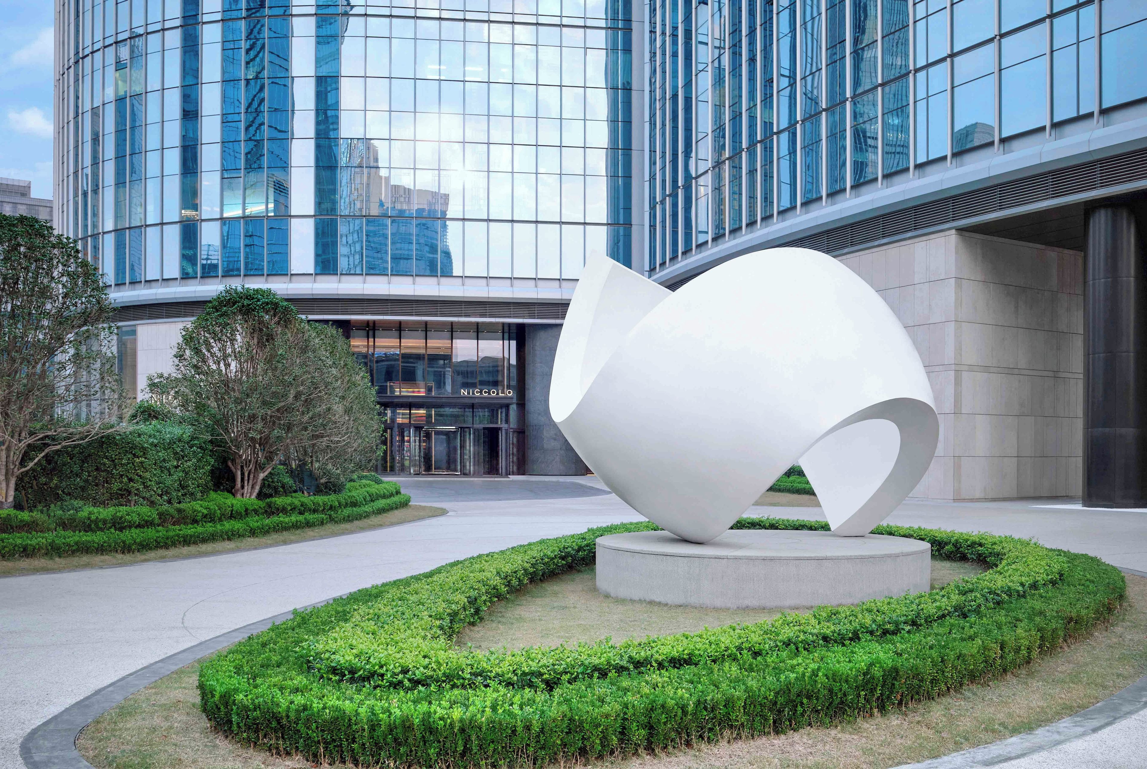 Un edificio moderno con fachada de vidrio y una escultura blanca distintiva al frente.
