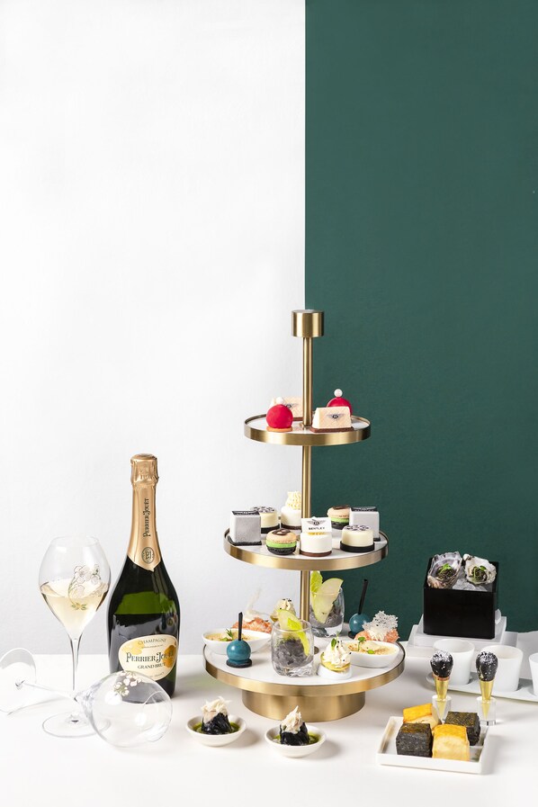 Un présentoir à gâteaux à plusieurs niveaux, garni de diverses pâtisseries et accompagné d’une bouteille de champagne.