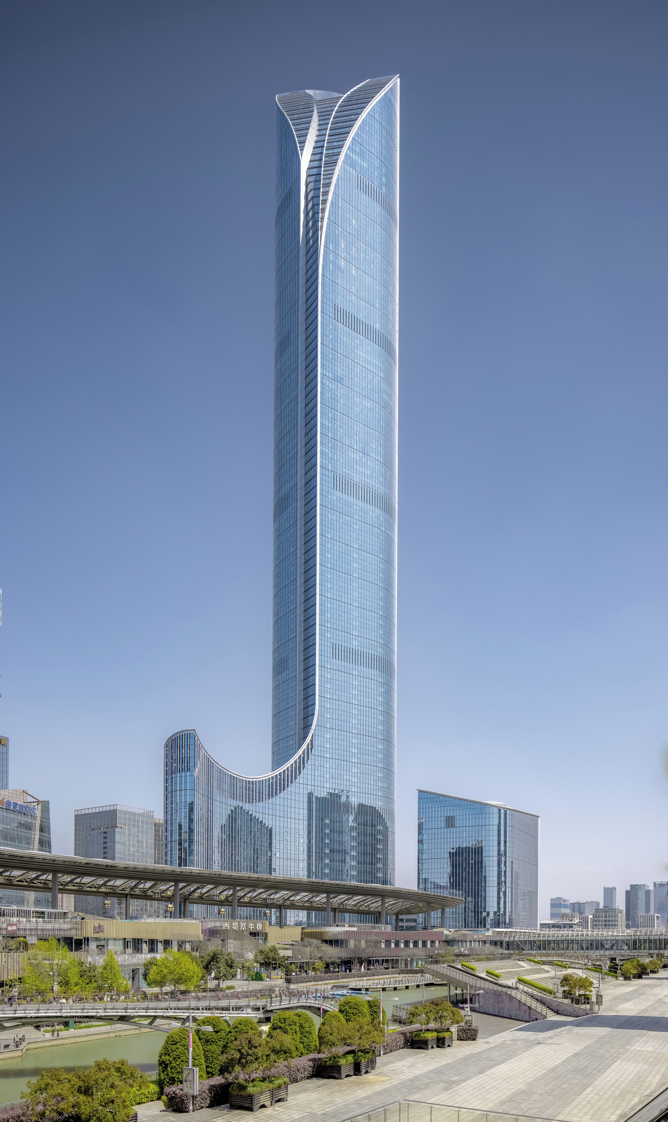 A modern skyscraper with a curved design, surrounded by other high-rise buildings and a river.