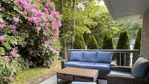 En overdækket terrasse med udendørs møbler i flet, en blå sofa og et træbord.