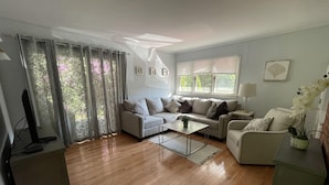En moderne stue med sofa, sofabord og fjernsyn på et stativ.