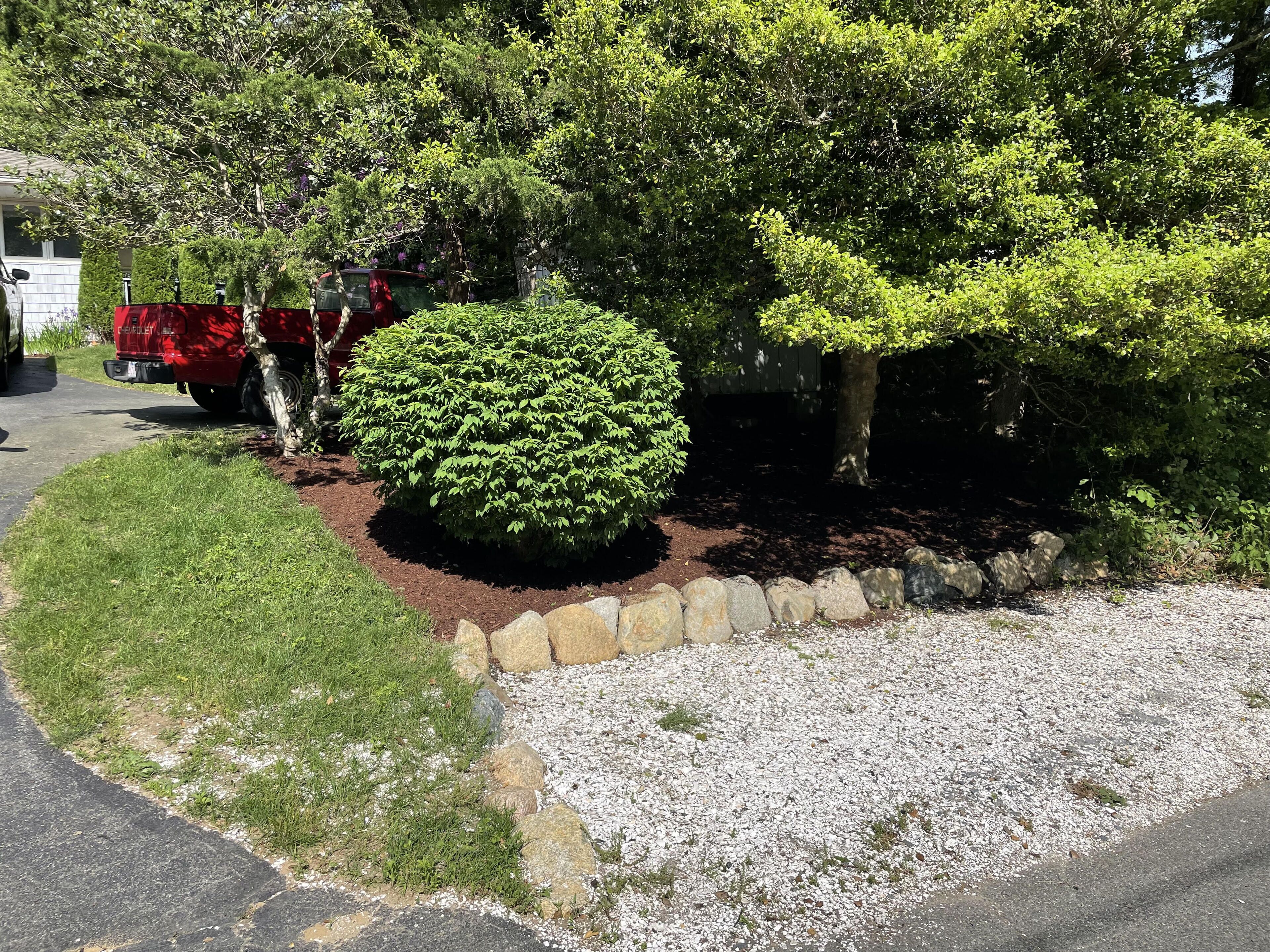 Un jardin aménagé avec des arbustes bien entretenus, une bordure en pierre et un chemin de gravier.
