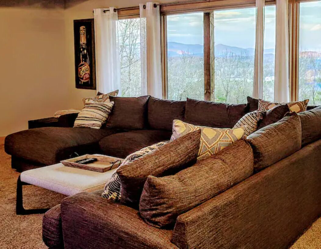 A living room with a large sectional sofa, a coffee table, and a view of mountains through large windows.