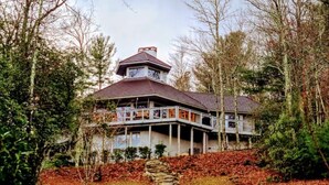 A large, multi-story house with a prominent tower, surrounded by trees and a stone pathway leading to the entrance.
