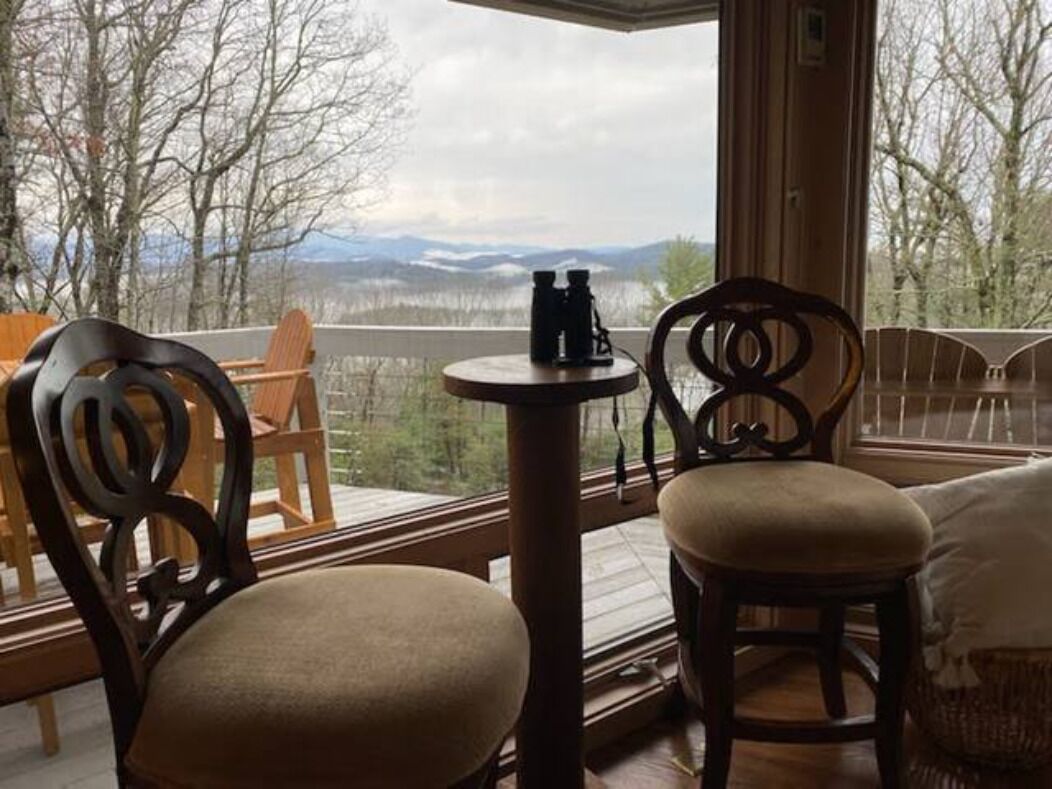 Ein Zimmer mit Blick auf die Berge, ein runder Tisch mit Fernglas und zwei Holzstühle.