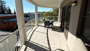 A balcony with a table and chairs, a view of buildings, and a clear sky.