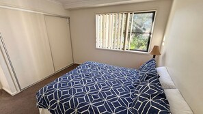 Une chambre à coucher avec un lit, une fenêtre avec des stores, une armoire et une lampe.