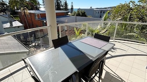 A balcony with a glass table and chairs, a view of buildings, and a tiled floor.
