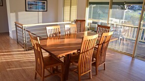 A dining area with a wooden table and chairs, a view of the outdoors through large windows, and a picture on the wall. - Amberlee House - South West Rocks (SOUTH WEST ROCKS)