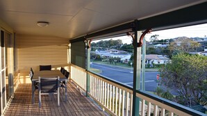 A wooden deck with a table and chairs, overlooking a street with houses and a stop sign. - Amberlee House - South West Rocks (SOUTH WEST ROCKS)