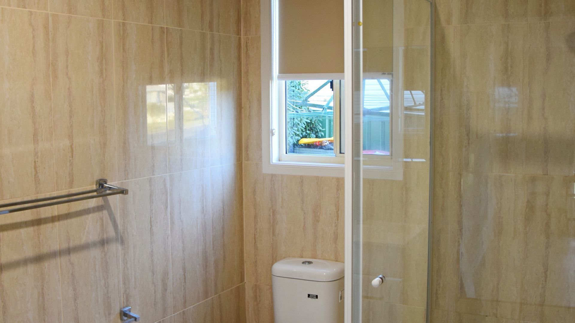A bathroom with a glass shower enclosure, a toilet, and a window with a view of the outside.