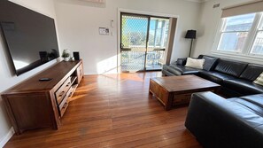 Un salon équipé d’un téléviseur à écran plat, de meubles en bois, d’un canapé en cuir et d’une porte-fenêtre coulissante donnant sur un espace extérieur.