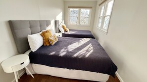 A bedroom with two beds, a nightstand, and a window.