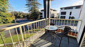 A balcony with a glass table and chairs, overlooking a street with cars and buildings.
