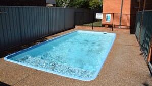 A rectangular swimming pool with a blue edge, surrounded by a gravel area and a metal fence. - Cameo Court Unit 7  - South West Rocks (SOUTH WEST ROCKS)