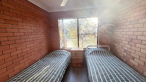 A room with two single beds, a window with a view of trees, and brick walls.