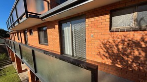 A building with a brick facade, large windows with metal grilles, and a balcony with a metal railing.