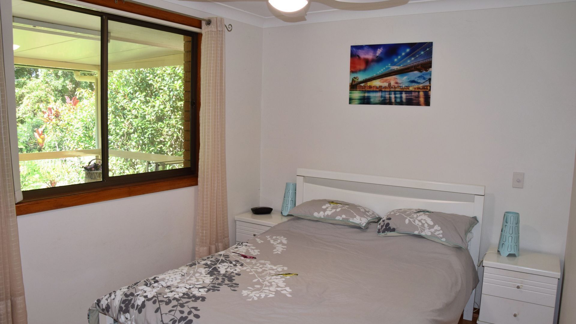 A bedroom with a bed, a nightstand, a window with curtains, and a wall-mounted picture.
