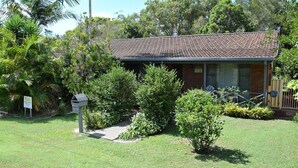 A small, single-story building with a tiled roof, surrounded by lush greenery and a well-maintained lawn. - Sunny Nook - South West Rocks - Bring your own linen (SOUTH WEST ROCKS)