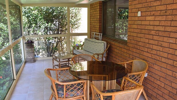 A covered patio with a glass table and wicker chairs, overlooking a lush garden. - Sunny Nook - South West Rocks - Bring your own linen (SOUTH WEST ROCKS)