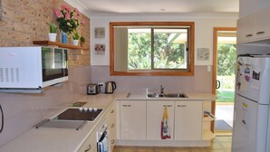 A compact kitchen with a microwave, toaster, sink, and a window overlooking greenery. - Sunny Nook - South West Rocks - Bring your own linen (SOUTH WEST ROCKS)