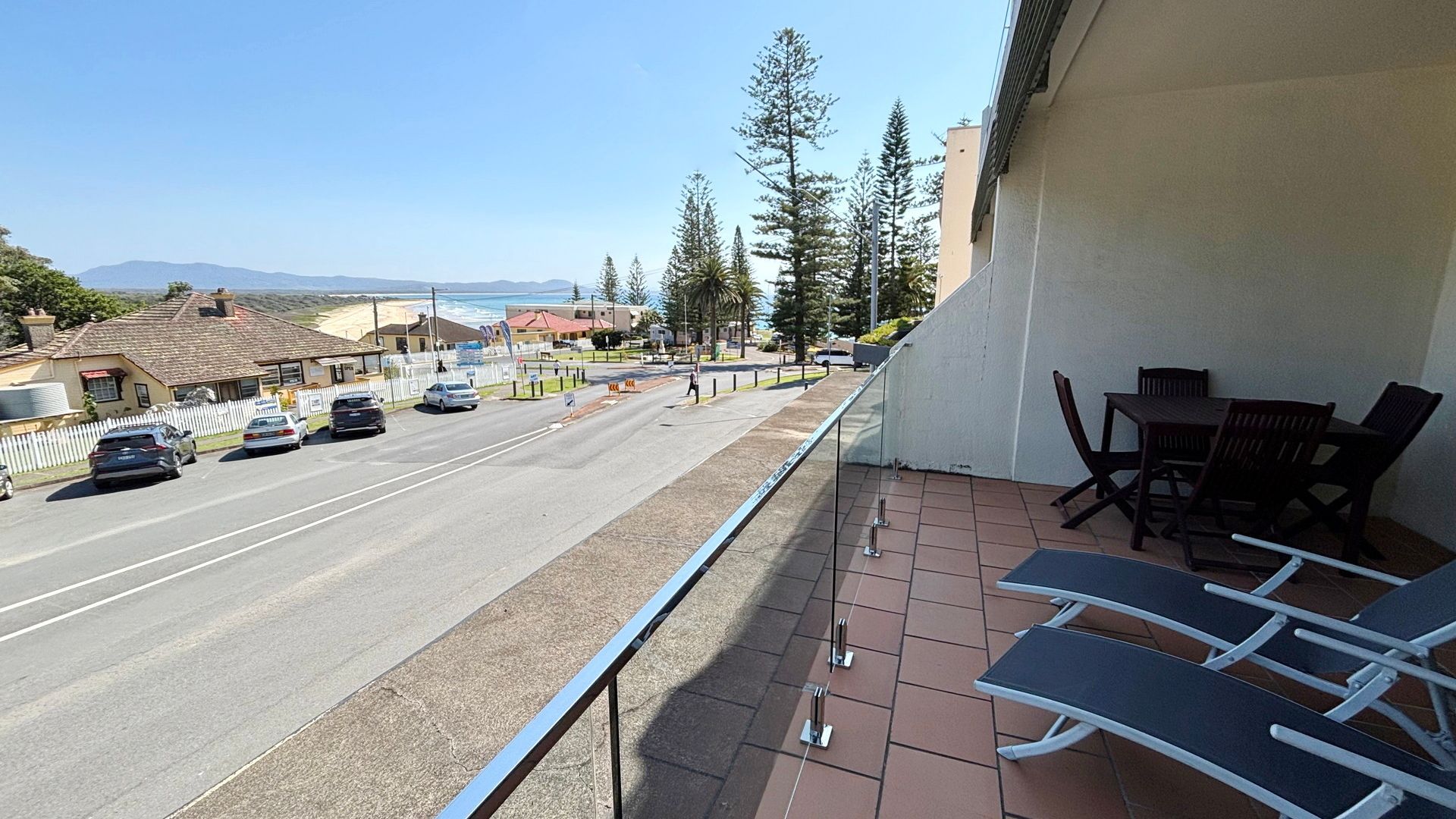 A balcony with a view of a road, parked cars, and a distant landscape.