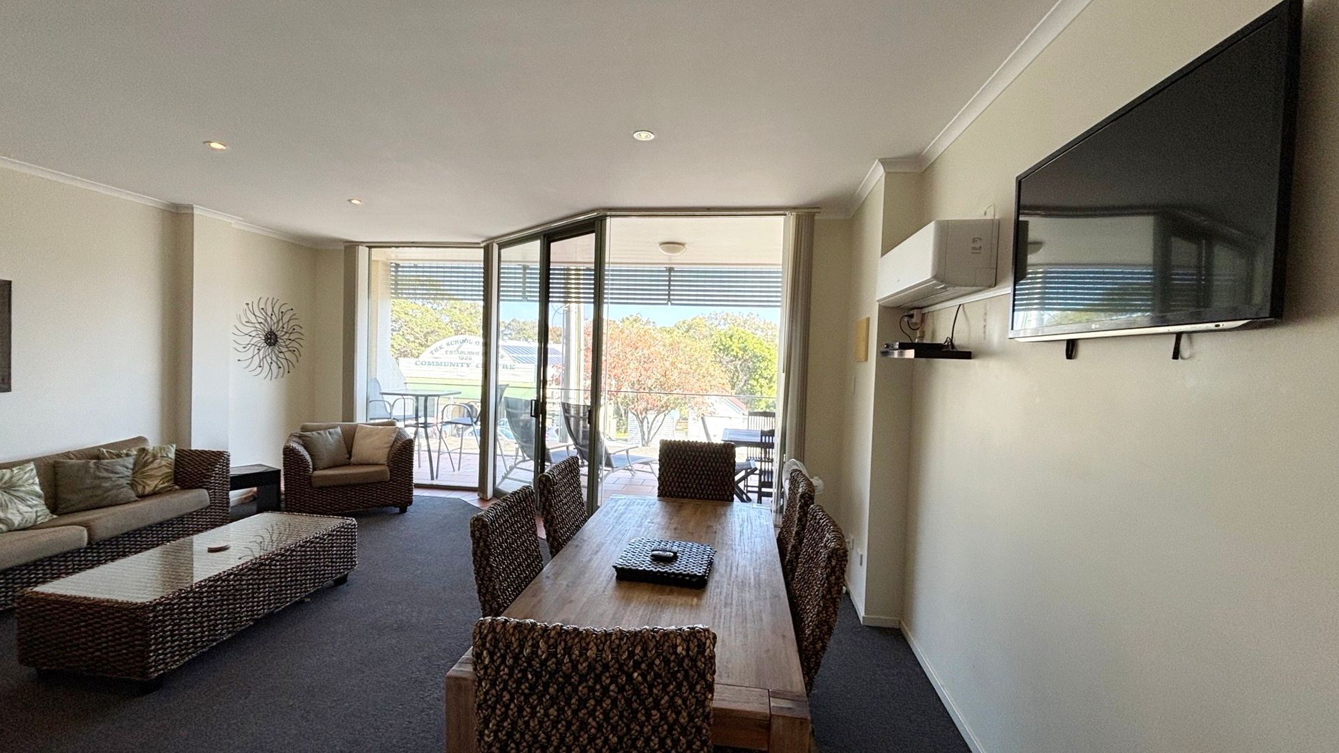 A living room with a sofa, chairs, a dining table, and a TV mounted on the wall.