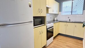 A compact kitchen with a refrigerator, microwave, stove, and cabinets. - Traveller's Palms # 7 - South West Rocks - Bring your own linen (South West Rocks)