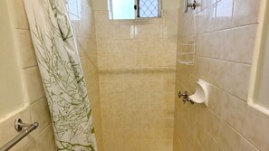 Een badkamer met beige tegels, een douchegordijn met bladmotief, een raam en een urinoir.