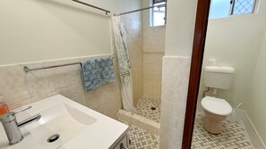 Een badkamer met douche, toilet en wastafel.