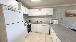 Een kleine keuken met witte kastjes, een roestvrijstalen koelkast, een magnetron en een spoelbak.