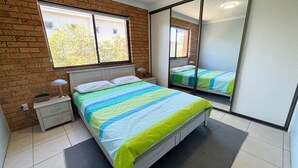 A bedroom with a bed, nightstands, a mirror, and a window. - Seacrest # 5  - South West Rocks (SOUTH WEST ROCKS)