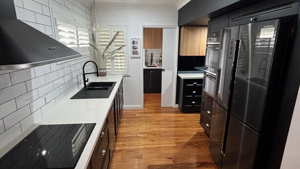 A modern kitchen with a black refrigerator, white tiled backsplash, and wooden flooring. - Landwin Gardens 1 - walk to the beach (SOUTH WEST ROCKS)