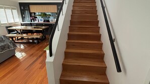 A wooden staircase with a black handrail leading to a dining area with a wooden table and chairs. - Landwin Gardens 1 - walk to the beach (SOUTH WEST ROCKS)