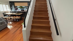 A wooden staircase with a black handrail leading to a dining area with a wooden table and chairs.